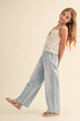 Young girl wearing a floral top and light blue jeans on a beige background