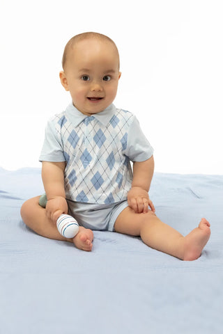 Baby sitting on a light blue blanket wearing a checkered shirt and shorts.