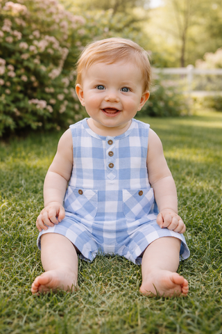 Baby sitting on grass wearing a blue checkered romper