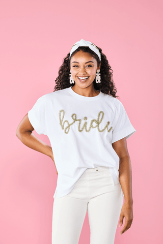 Woman wearing a white t-shirt with 'bride' in gold letters against a pink background