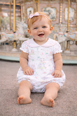 Baby in a white floral dress sitting on a carousel.