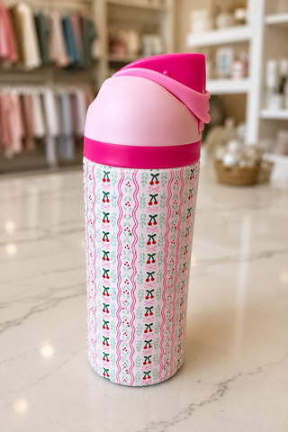 A pink and white patterned insulated water bottle with a bright pink lid, sitting on a light marble countertop in a softly blurred boutique setting.