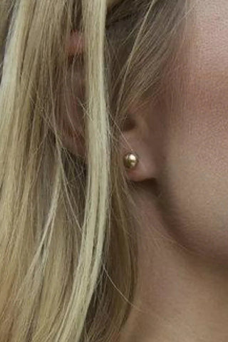 Close-up of a person wearing a gold earring with blonde hair.