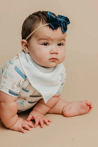 Baby wearing a blue bow headband and patterned outfit on a beige background