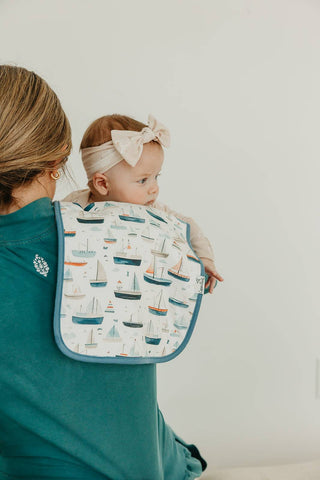 Baby being held by a person with a burp cloth with a boat pattern on their shoulder against a white background