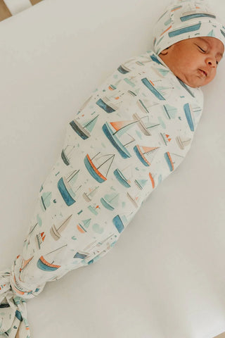 Newborn baby swaddled in a blanket with boat patterns on a white surface