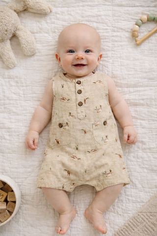 Baby wearing a patterned romper lying on a textured surface with toys around