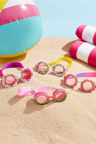 Colorful swim goggles on sand with pool float and towel in background