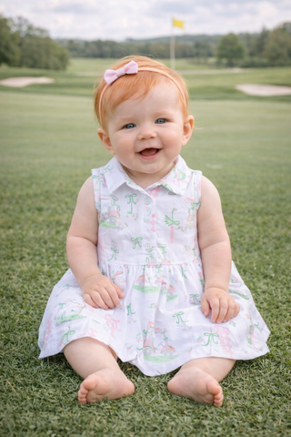 Baby in a floral dress sitting on grass with a golf course background