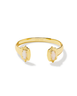 A gold cuff bracelet with two open ends, each decorated with a shield-like frame holding a pale pinkish-white oval stone. The brand name 'KENDRA SCOTT' is engraved inside the band.