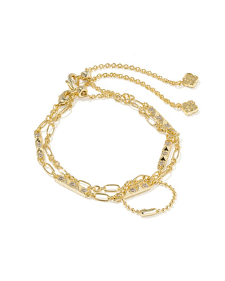 A gold-toned multi-strand bracelet featuring a barbell-style main chain, delicate chain links, small clear crystal accents, and two clover-shaped charms, displayed on a clean white background.