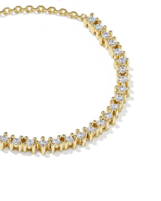 A close-up of a gold tennis necklace with clear round-cut stones in a prong setting, arranged in an arc on a white background.