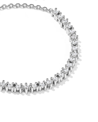 A close-up of a gold tennis necklace with clear round-cut gemstones in a prong setting, arranged in an arc on a white background.