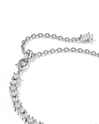 A close-up of a silver-toned chain bracelet with a row of clear stones along one side and an adjustable lobster clasp with a small charm at the end, shown on a white background.