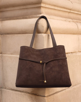 Brown leather handbag with gold clasp on a beige stone wall background