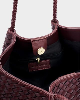 Close-up of a maroon handbag with braided handle and woven texture.