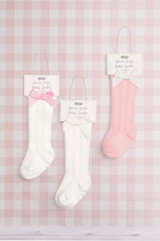 White and pink baby socks with tags on a pink checkered background