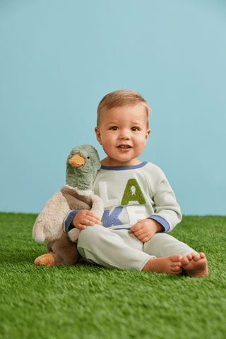 Child holding a plush duck toy on grass with a blue background