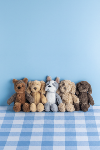 five stuffed dogs sitting on a blue and white gingham tablecloth in front of a blue wall.