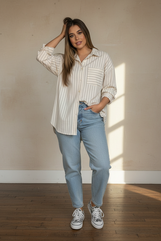 Woman wearing a striped shirt and jeans standing in a room with sunlight casting shadows on the wall.