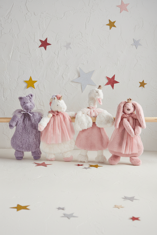 Four plush toys in dresses on a wooden surface with star decorations in the background.
