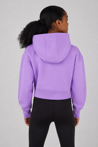 A person shown from the back wearing a cropped lavender-purple hoodie and black leggings against a light gray studio background.