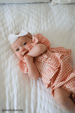 Baby in a checkered outfit lying on a white textured surface