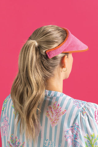 Person wearing a pink visor with a floral patterned shirt on a pink background