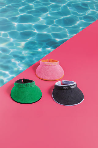 Three visors in green, pink, and black on a pink background with water in the corner.
