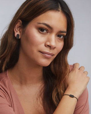woman wearing black druzy earrings and bracelet in front of a blue background 
