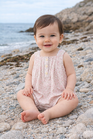 Baby sitting on a rocky beach with ocean in the background