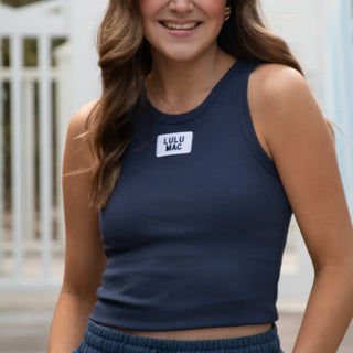 Woman wearing a navy blue tank top with 'LULU MAC' logo, standing outdoors.