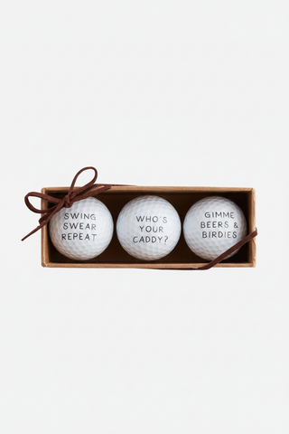 Three golf balls with humorous text in a cardboard box on a white background